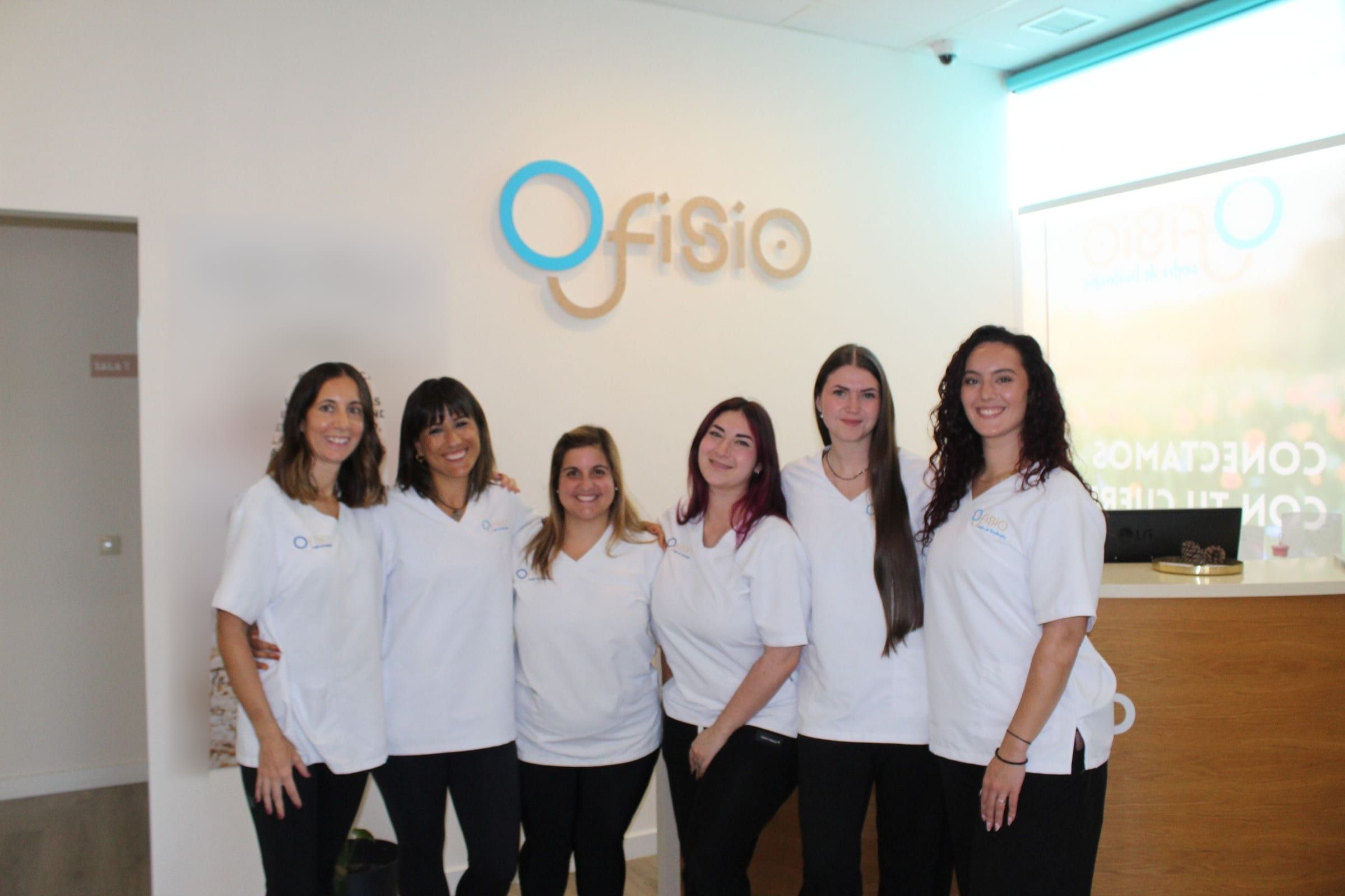Las seis profesionales de Ofisio con uniforme blanco posando juntas en la recepción, bajo el logo de la clínica