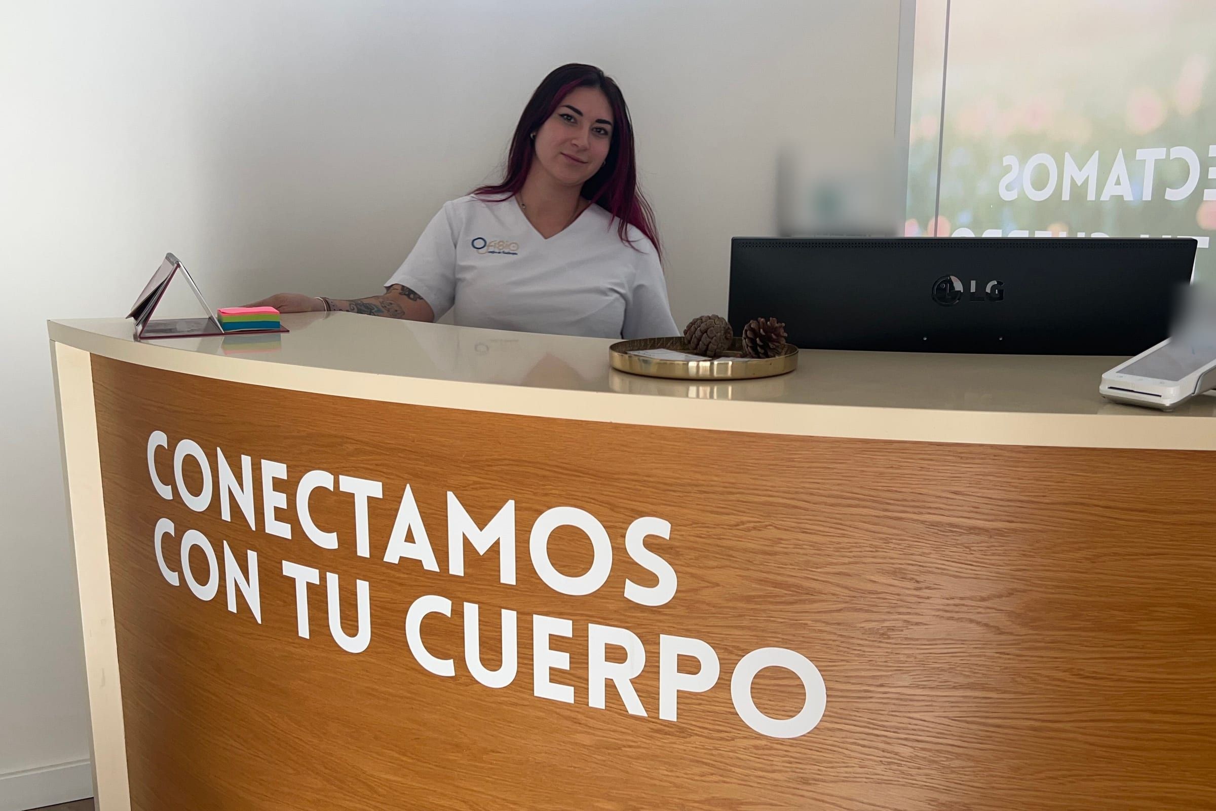 Recepción de Ofisio: una profesional de la clínica tras el mostrador con el lema «Conectamos con tu cuerpo»